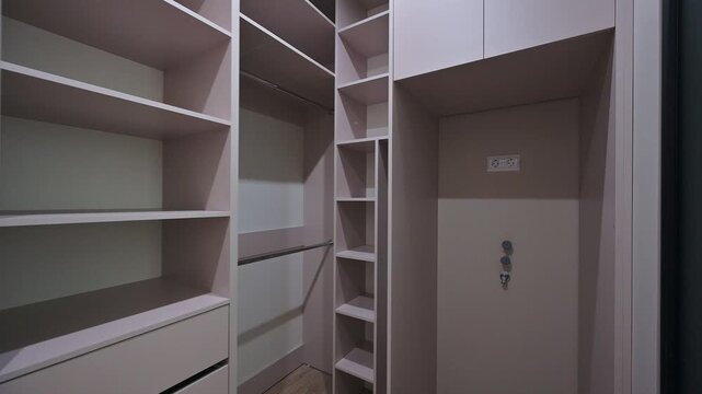 A modern built-in wardrobe with open shelves, drawers, hanging rails, and angled compartments in neutral tones &mdash; sleek, functional, space-saving design.
