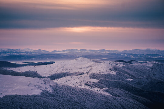 Winter mountain landscape during blue hour sunrise with snowy ridges and distant peaks of the Bieszczady Mountains, seen from Tarnica during frosty trekking conditions.
