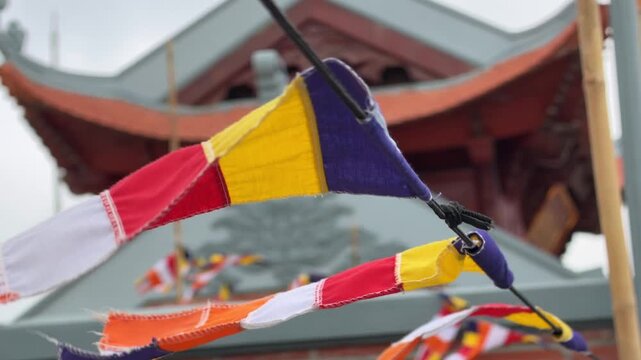 Buddhist flags stretch near a pagoda roof, with temple structures and open sky behind, showing colorful fabric lines across the sacred space. Pagoda flags.