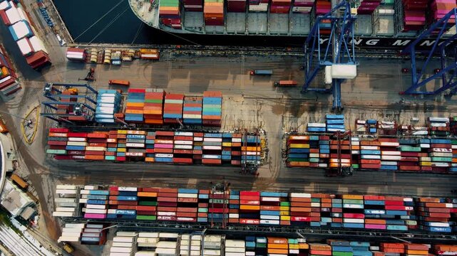 Top-down aerial drone view of a busy container port terminal with stacked shipping containers, cargo ship and cranes. Global trade, logistics, maritime transport and industrial infrastructure concept.