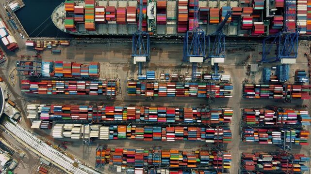 Top-down aerial drone view of a busy container port terminal with stacked shipping containers, cargo ship and cranes. Global trade, logistics, maritime transport and industrial infrastructure concept.