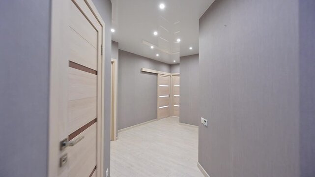 A sleek, light-gray hallway with recessed ceiling lights, light wooden doors, and a modern coat rack with hooks &mdash; minimalist and functional design.
