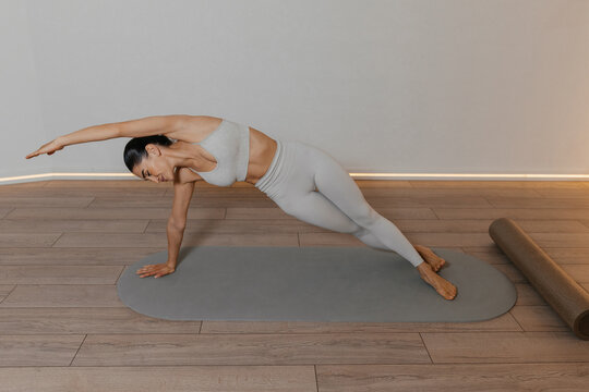Athletic woman holds side plank pose Vasisthasana with one arm supporting body and other arm extended forward. full body control in yoga and Pilates training