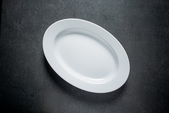A pristine white oval plate rests on a textured dark surface, inviting culinary creativity