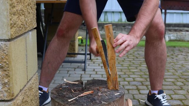 A man splits a log vertically with an axe on a stump in a courtyard, preparing firewood for grilling or outdoor cooking.
