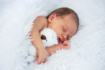 Newborn baby sleeping and hugging a white crocheted teddy bear toy