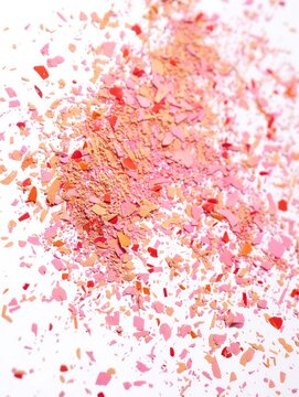 Colorful crushed makeup powder scattered on a white surface, showcasing various shades of pink, peach, and red. Beauty and cosmetics concept.