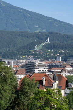Scenic urban view of Innsbruck featuring the iconic Bergisel ski jump with a backdrop of dense forests and Alpine mountains