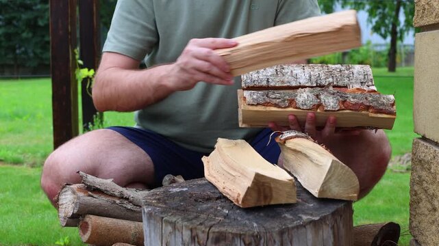 A person arranges split firewood, birch and hardwood, on a log stump outdoors, preparing for grilling or smoking.