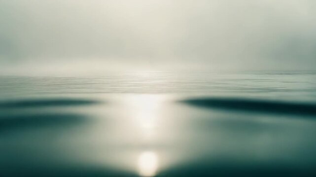 Calm mist hangs over a tranquil water surface, creating an ethereal minimalist seascape with soft, diffuse light, gentle ripples and wide empty horizon for copy space