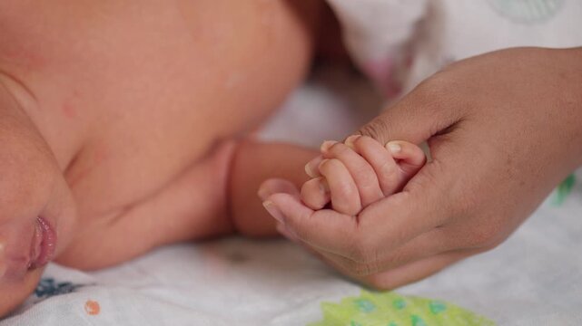 Newborn baby holds adult finger tightly. A symbol of unconditional love, bonding, and emotional connection.