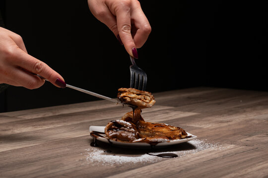 crepe o panqueque relleno con manjar, espolvoreado  con az&uacute;car flor y ba&ntilde;ado en salsa de chocolate, cortado con cuchillo y tenedor