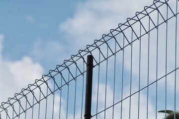 Fototapeta premium Security Fence With Curved Wire Top Against Blue Sky and Clouds