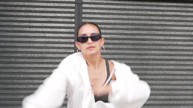 Attractive young woman with sunglasses dancing and grooving in front of a metal rolling shutter