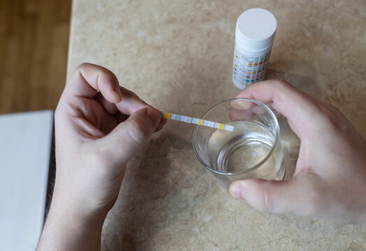 A man in the kitchen tests tap water quality with a test strip. Home testing for drinking water safety, pH, chlorine, and chemical contaminants.