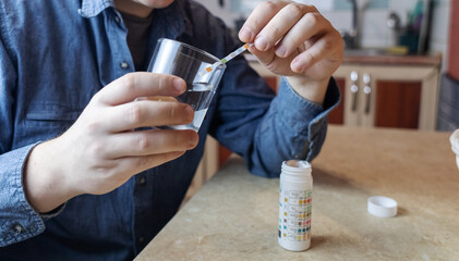 A man in the kitchen tests tap water quality with a test strip. Home testing for drinking water safety, pH, chlorine, and chemical contaminants. © Siniehina
