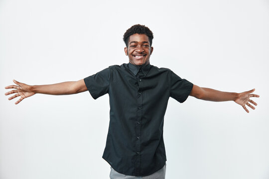 Young black man with dark skin wearing black shirt smiling with arms wide open on white background for happiness and positivity concept.