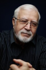 Obraz premium Elderly man with glasses sits thoughtfully in a dark room during evening hours while reflecting on past experiences