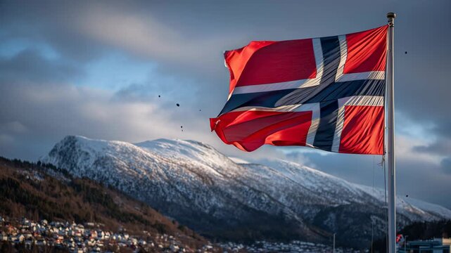 Norwegian flag waving against a backdrop of beautiful snow covered mountains, a small village, and dramatic cloudy sky, embodying national pride and the stunning scandinavian landscape