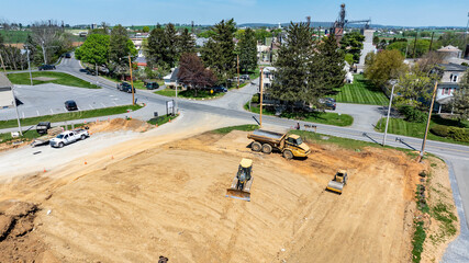 Heavy machinery is present at a construction site in a rural area. Workers use a bulldozer and a...