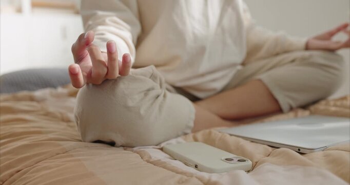 Close up. teenage female hands in mudra pose meditating on bed, digital detox concept with smartphone and laptop ignored in background