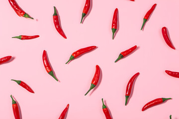 Chili peppers scattered on pink background with varied spacing and arrangement in daylight