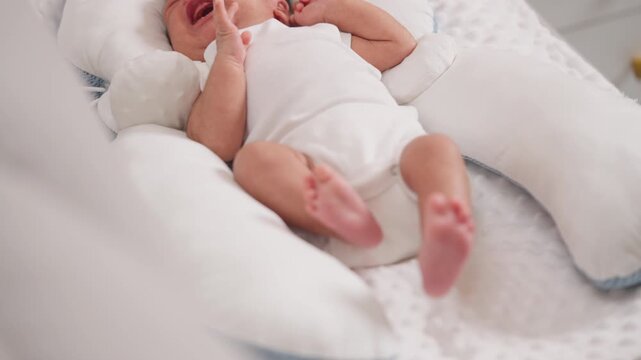 Asian newborn baby crying while lying on soft white cushion, showing emotional moment and real-life parenting challenge.