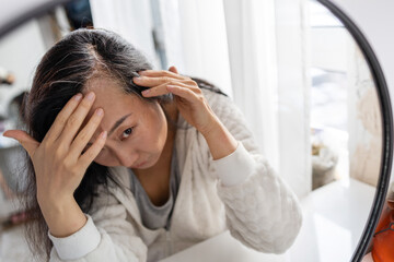 Sad Asian middle aged woman having her hair trouble in the living room.