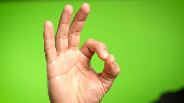 Hand forming the OK gesture sign, expressing approval or affirmation against a vibrant green background