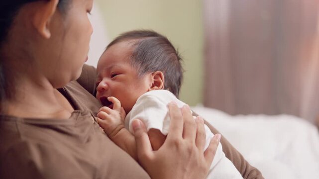 Mother holds baby upright for burping after feeding. Reflects baby care routine and loving parenting moments.