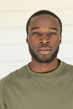 African American adult man standing facing camera against light paneled wall in olive crewneck tee