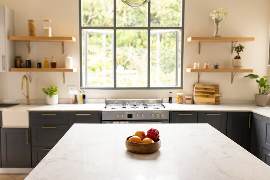 Wooden fruit bowl is sitting on white marble island, holding three oranges and red dragon fruit