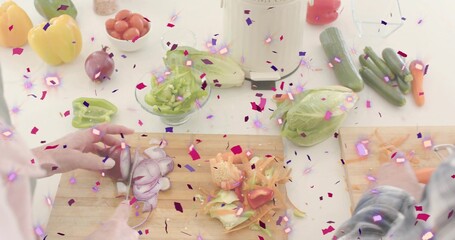 Slicing two hands in light sleeves, plaid, chopping carrots and onion on counter with confetti