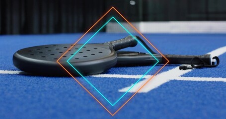 Lying two black paddles resting flat on blue court, with white line and neon diamond overlay