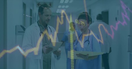 Reviewing lab-coat doctor and nurse in scrubs with tablet and folder in ward, with financial graphs