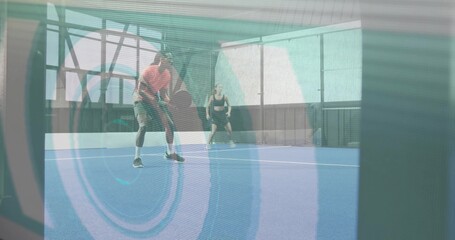Fototapeta premium Holding paddle, male in orange and female in black tank preparing return shot inside covered court