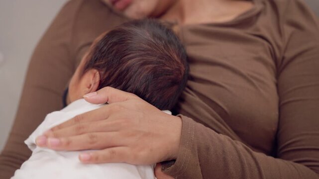 Mom cradles newborn baby gently against her chest. Classic pose of motherhood, comfort, and unconditional love.