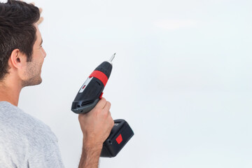 Cordless drill is pointing at white wall on left, thin bit and battery visible, copy space