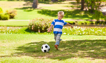 Boy child kicking black-and-white soccer ball barefoot in park wearing striped T-shirt faded jeans