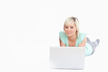 Woman in her twenties lying on seamless white studio floor using silver laptop, copy space