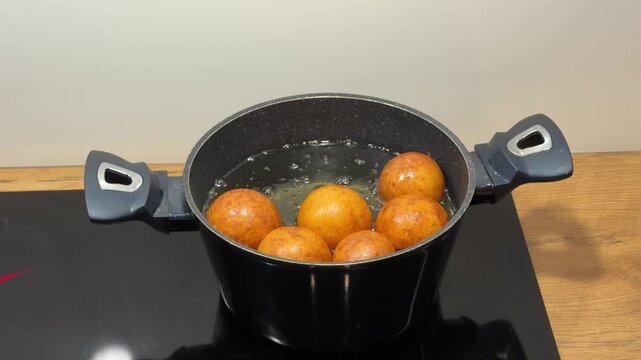 Round Dough Balls Bubbling in Pot of Hot Cooking Oil. Several perfectly round pieces of dough fry in oil creating active bubbling on surface. Snacks turn deep golden color as they cook on stove.