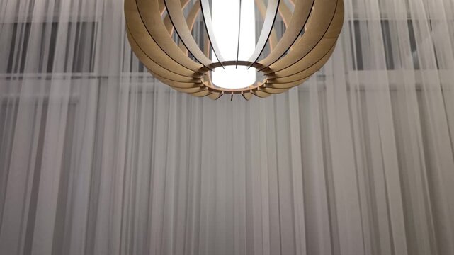 Modern Wooden Pendant Light Panning to Minimalist Dining Setup. Camera pans down from stylish wooden geometric chandelier to wooden dining table set with woven placemats and vase with dried grass.