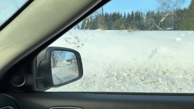 POV Car Trip Through Hilly Snowy Neighborhood. Driving along winding road through snowy residential area with houses on hillsides. Route surrounded by tall evergreen trees and high snowbanks.
