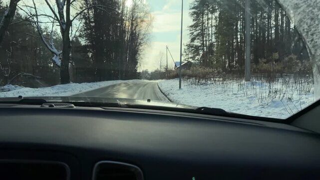 Driving Through Sunlit Winter Forest at Midday. Perspective from car moving along winding road through dense snow-covered forest. Bright sunlight filters through trees creating sparkling winter vibe.