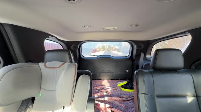 Rear View from Inside Moving Car on Winter Road. Static interior shot looking out back window of car traveling on snowy road. Sunlight streams in illuminating black leather seats and blanket in cargo.