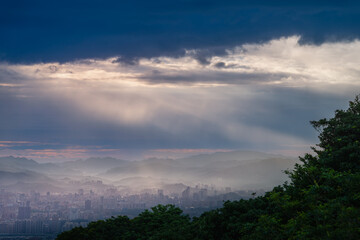 Fototapeta premium Stunning view from Dadao Mountain Shulin Taiwan. Dramatic light rays penetrate rain clouds over Taipei city skyline creating mystical atmosphere.
