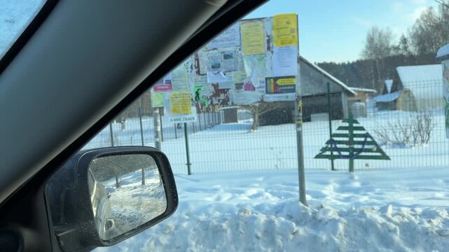 Passing Little Free Library and Notice Board in Winter. View from car passing rural community spot with notice board and small free library box. Wooden Christmas decorations stand in snow.