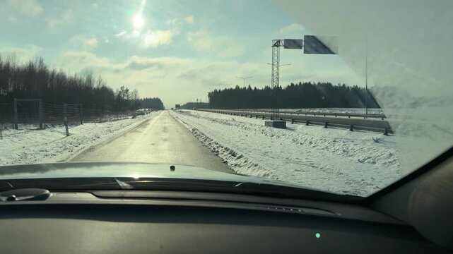 Highway Driving in Winter with Overhead Signs. POV driving shot on major road in winter approaching overhead traffic signs. Sun is bright illuminating wet asphalt and high snowy banks on shoulder.