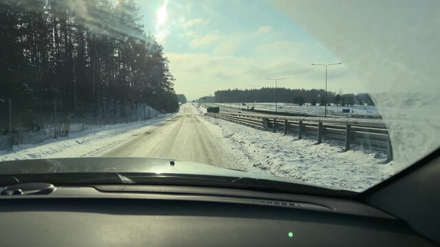 Driving on Winter Highway with Sun Glare. POV driving shot on plowed highway during sunny winter day. Bright sun creates glare on windshield as car passes guardrails and snow banks.