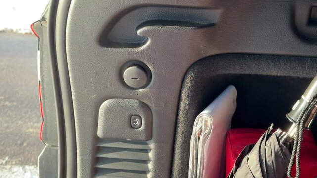 Pressing Automatic Trunk Button Inside Car. Close-up shot of finger pressing automatic close button located inside trunk of vehicle. Black plastic button features car icon.